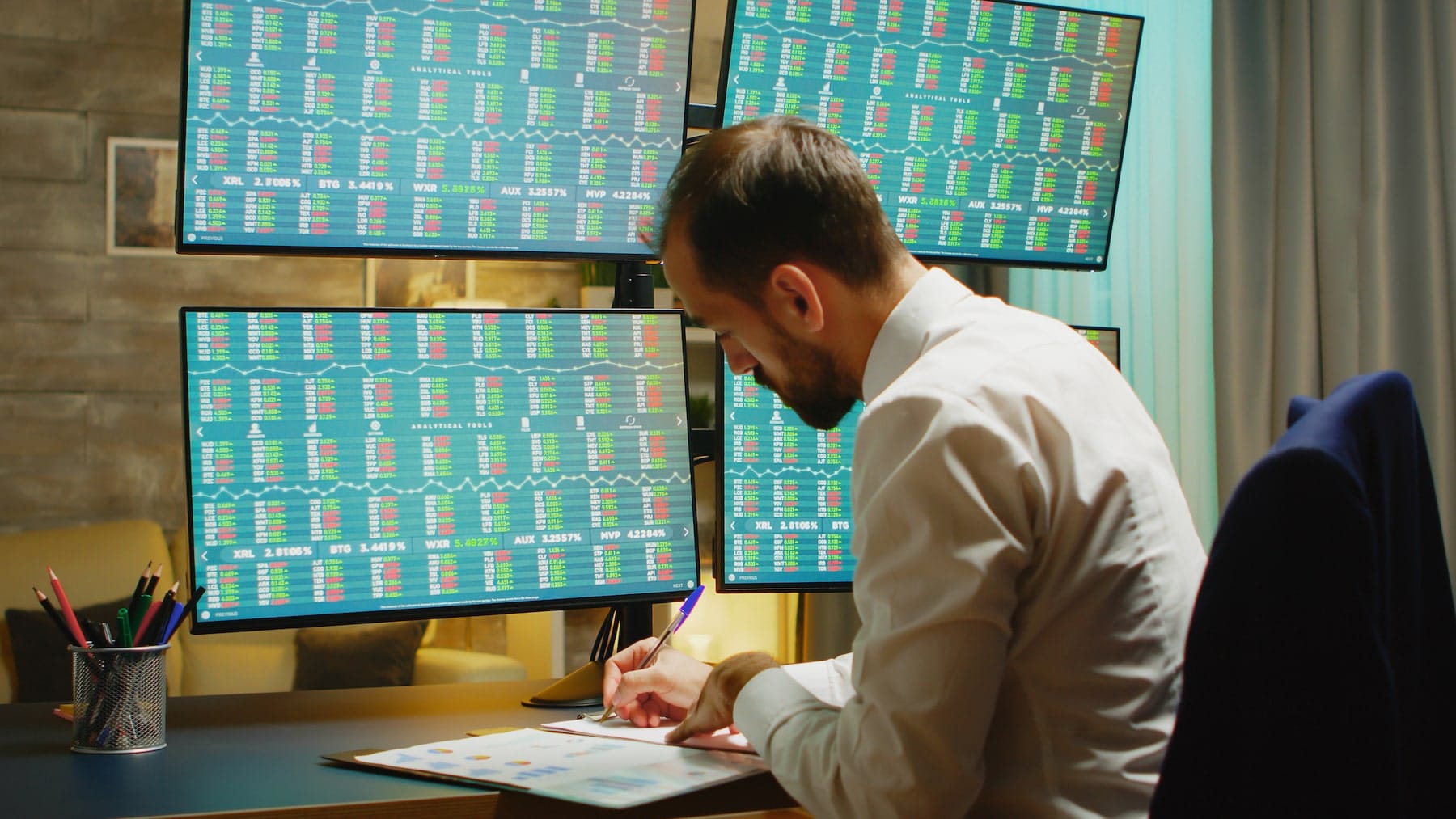 bearded businessman taking notes while checking stock market from home office min